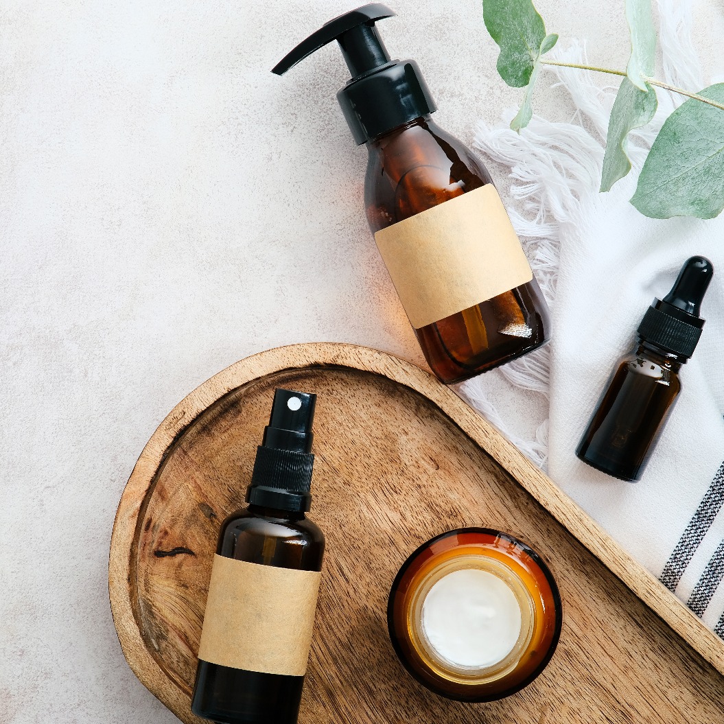 Set mit natürlichen Bio-SPA-Schönheitsprodukten auf einem Holzbrett mit Eukalyptusblättern. Kosmetikflaschen aus Braunglas in der Draufsicht.